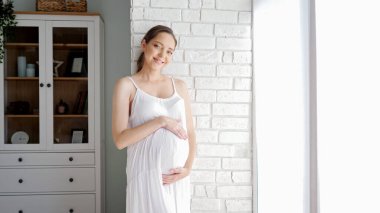 Müstakbel anne odada tuğla duvarın yanında duran karnına dokunuyor.