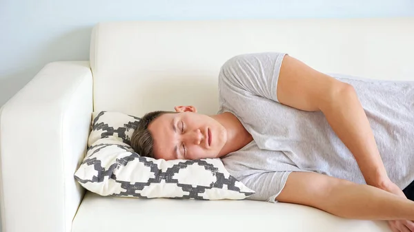 Втомився молодий чоловік падає на диван з подушкою в кімнаті — стокове фото