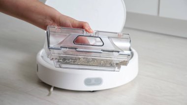 Kadın, robot süpürge kutusunu çöp kutusuyla açıyor.