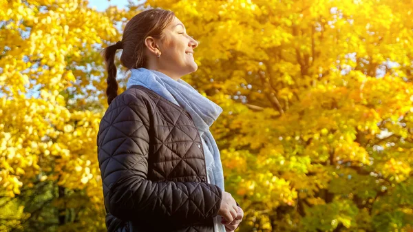 Giovane donna bruna sorridente al sole sullo sfondo di alberi gialli di autunno — Foto Stock