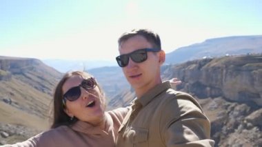 Güneş gözlüklü mutlu çift dağlara karşı selfie çekiyor.