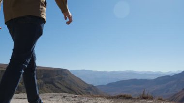 Mavi gökyüzünün altında çift yürüyor ve el ele tutuşuyor.