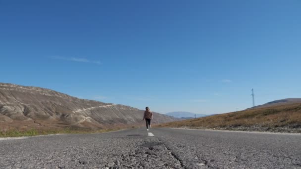 Jonge vrouw rent langs weg tegen heuvels en blauwe lucht — Stockvideo