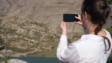 Beyaz gömlekli kadın, sakin gölü olan vadinin fotoğrafını çekiyor.
