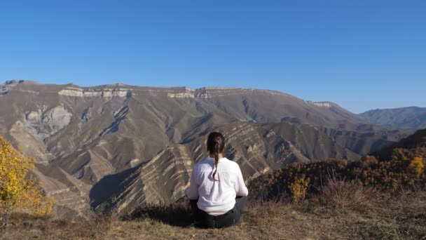 Frau meditiert sitzend am Bergrand vor großen Bergen — Stockvideo