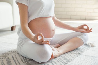 Evde çıplak karnına meditasyon yapan hamile bir kadın.