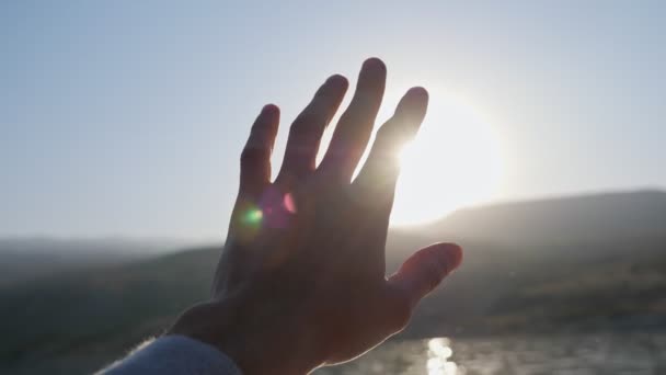 El hombre toma de la mano tratando de ocultar el sol brillante en el cielo azul claro — Vídeos de Stock