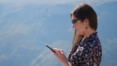 Güneşli bir günde, arka planda telefonla dolaşan genç bir kadın. Rüzgarda dalgalanan saçlar.