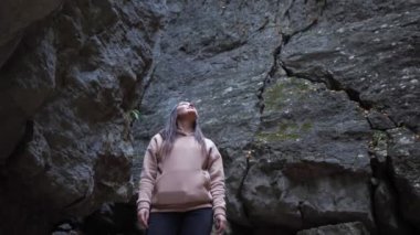 Kapüşonlu esmer kadın kayalık bir vadide yukarı bakıyor.