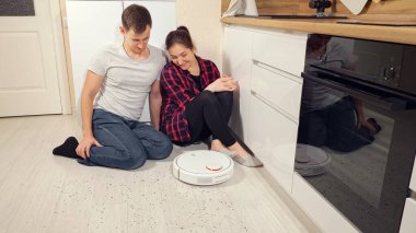 Çift, robot elektrik süpürgesinin çöpü çıkarmasına bakıyor.