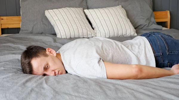 Уставший парень падает на кровать с серым бельем и подушками — стоковое фото