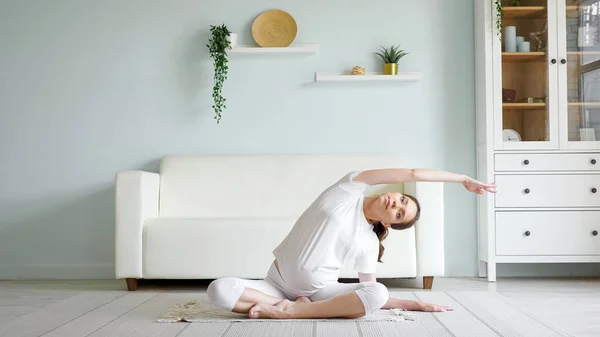 Brunette pregnant woman does side bends on floor at home — Stock Photo, Image