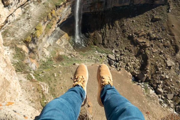 Человек в джинсах и кроссовках сидит на скале, размахивая ногами. — стоковое фото