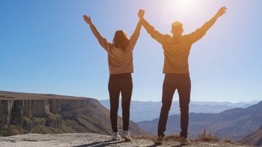 Mavi gökyüzünün altında çift yürüyor ve el ele tutuşuyor.