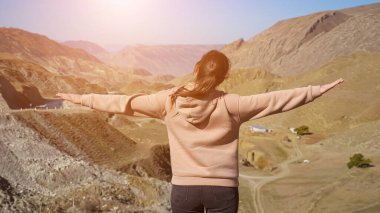 Dağlarda kapüşonlu bej ve pembe kazaklı bir kadın.