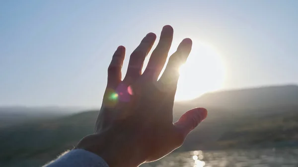 L'homme tient la main en essayant de cacher le soleil brillant dans un ciel bleu clair — Photo
