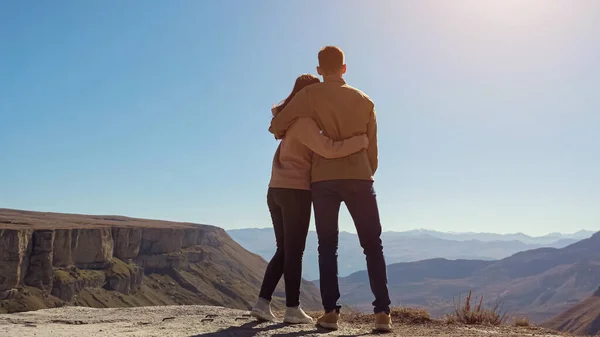 Mladý pár zamilovaný přes útes obdivuje výhled na údolí za jasného slunečného dne — Stock fotografie
