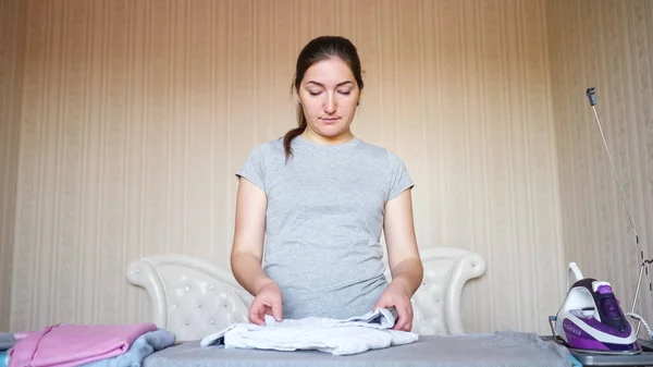 Relaxed dark haired housewife stacks clothes after ironing — Stock Photo, Image