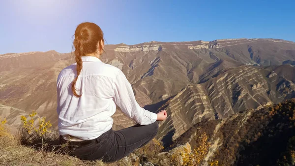 Signora con treccia medita sulla scogliera contro montagne lontane — Foto Stock