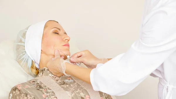 O doutor insere uma agulha em uma cara de mulher subcutaneamente close-up — Fotografia de Stock
