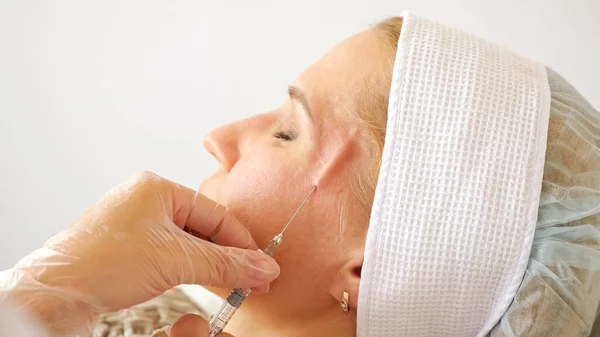 Beautician inserts a long needle with medication under the skin of a womans face