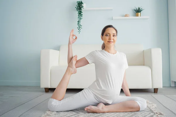 Smiling young pregnant brunette woman practices yoga on floor at home — Stock Photo, Image