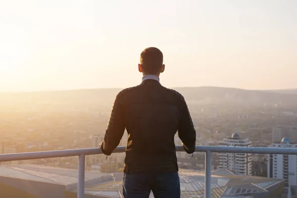 Muscular man admires sunrise over cityscape and hills