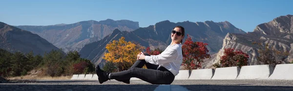 Junge Frau mit Sonnenbrille sitzt auf Barriere gegen Berge — Stockfoto