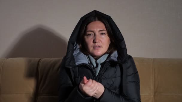 Дама в теплій куртці з капюшоном намагається нагріти руки на дивані — стокове відео