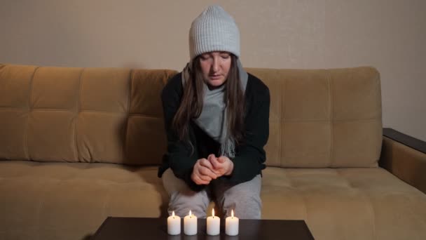 Mulher congelada tenta aquecer as mãos sobre a queima de velas no sofá — Vídeo de Stock