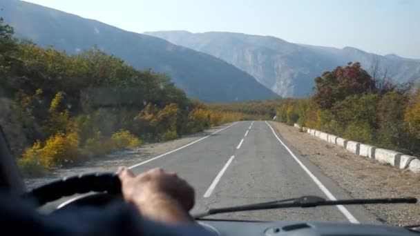 Guidare lungo la strada tra alberi autunnali contro le montagne — Video Stock