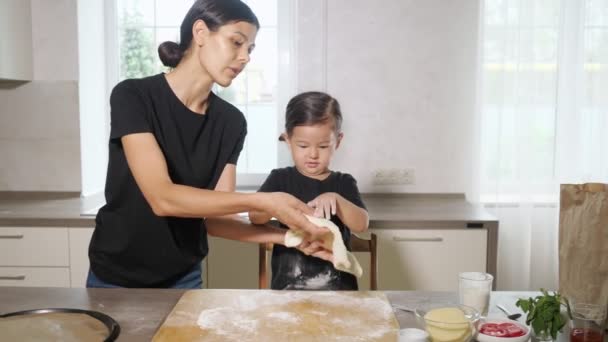 Malá holka hraje s těstem v přítomnosti maminky v kuchyni — Stock video