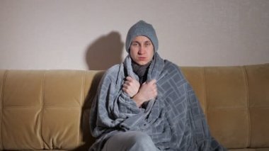 Donmuş adam modern kanepede otururken soğuktan titriyor.