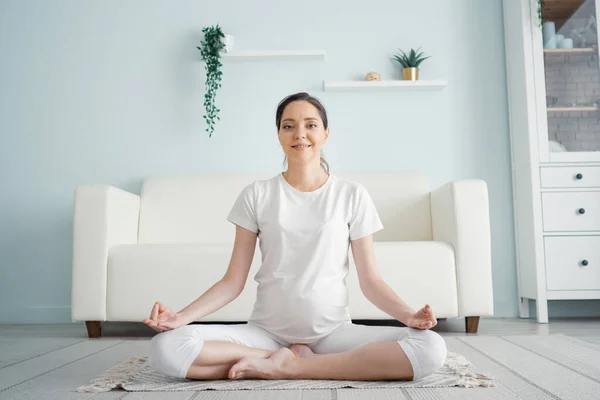 Young pregnant lady meditates sitting in padmasana on floor — Stock Photo, Image
