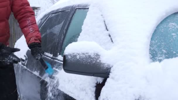 Onherkenbare man reinigt een auto van sneeuw met een blauwe borstel — Stockvideo