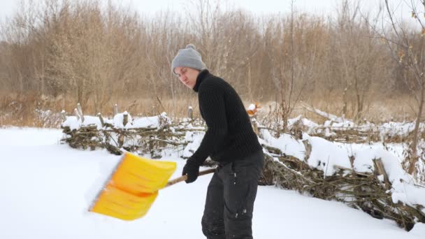 Молодий чоловік очищає сніг жовтим пластиковим лопатою в повільному русі — стокове відео