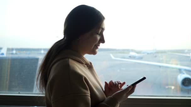 Close-up of a young woman with a phone against the background of a window in an airplane view — Stock Video