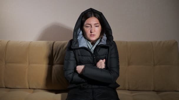 Dame in warmer Jacke mit Kapuze versucht Hände auf Sofa zu erwärmen — Stockvideo