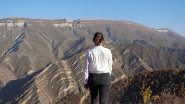 Mujer joven camina y levanta las manos contra las montañas — Vídeos de Stock