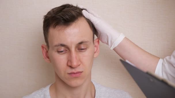 Médico con guantes examina la cabeza de un hombre calvo y llena una tarjeta de historial médico — Vídeos de Stock