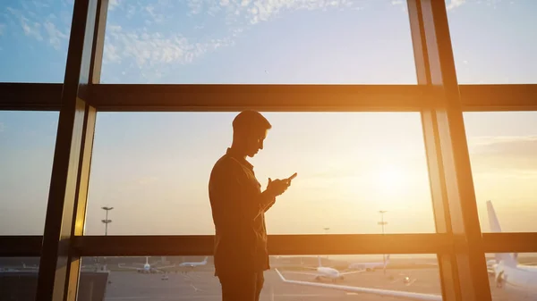 Мужчина заходит в интернет со смартфоном у окна в аэропорту — стоковое фото