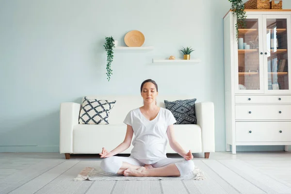 Young pregnant lady meditates sitting in padmasana on floor — Stock Photo, Image