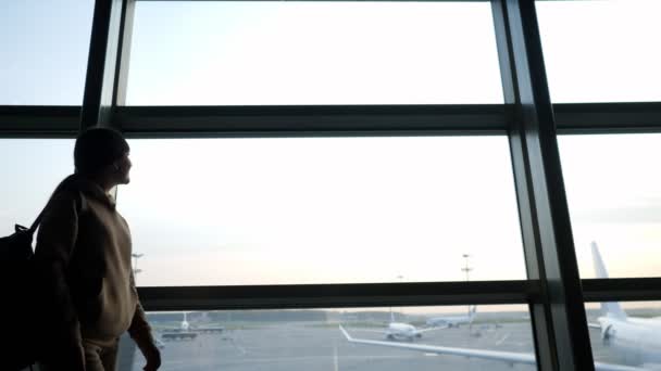 Młoda kobieta z plecakiem przechodzi obok panoramicznego okna na lotnisku — Wideo stockowe