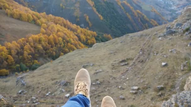 La persona se sienta balanceando las piernas en el alto acantilado sobre el valle verde — Vídeos de Stock