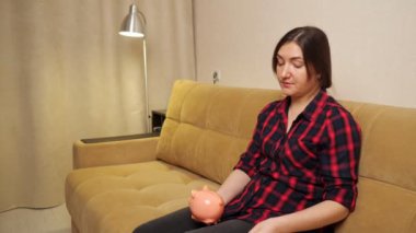 Kadın elinde kumbarayla kanepeye oturur ve bozuk para atar.