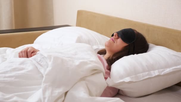 Jovem mulher vestindo máscara de dormir encontra-se relaxado na cama moderna — Vídeo de Stock