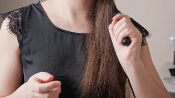 Tânăra femeie rulează pieptene de-a lungul părului castaniu închis și arată perie — Videoclip de stoc