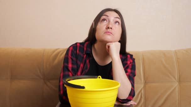 Эмоциональная женщина собирает воду в ведро, сидя на диване — стоковое видео