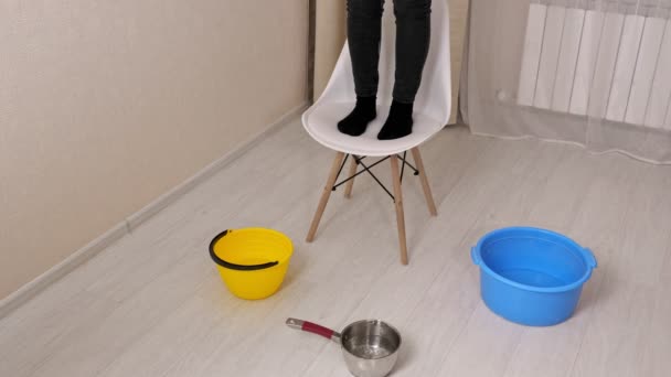 Woman stands on chair by containers collecting coming water — Stock Video