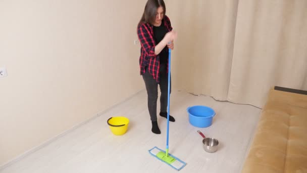 Verstoorde vrouw dweilt natte vloer met wastafels in lichte woonkamer — Stockvideo